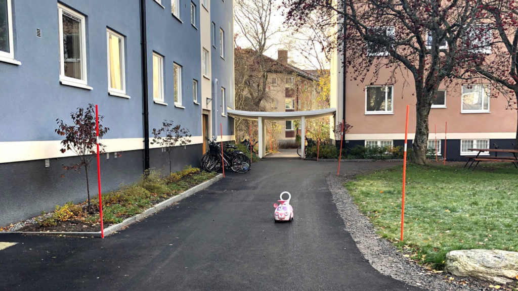 Foto på två lägenhetshus. På gångvägen utanför står en leksaksbil för barn.