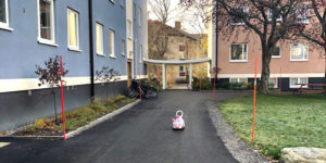 Foto på två lägenhetshus. På gångvägen utanför står en leksaksbil för barn.