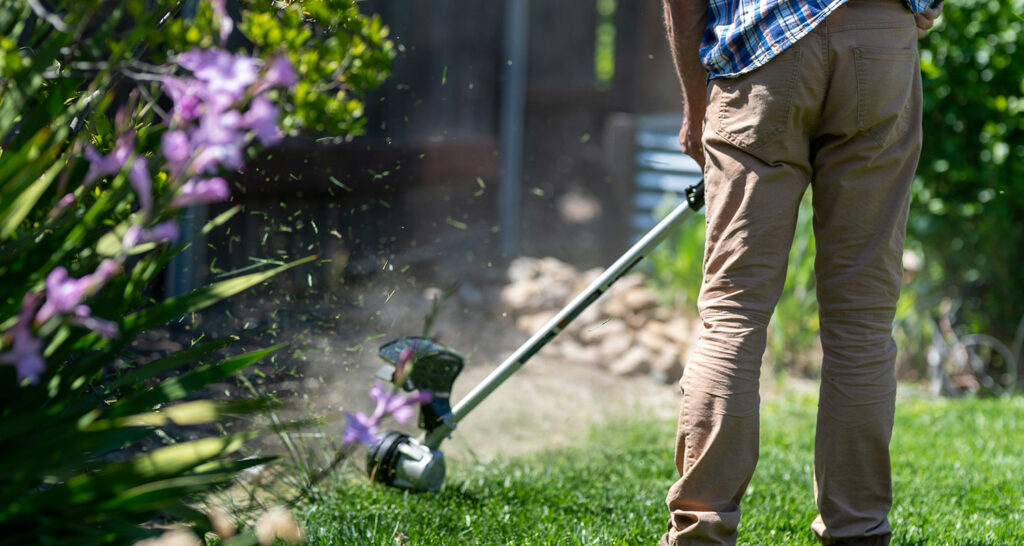 En person med grästrimmer i en trädgård, ansar en gräskant.