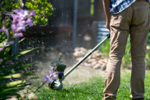 En person med grästrimmer i en trädgård, ansar en gräskant.