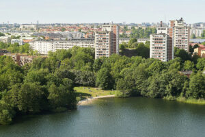 En vy över bostadsområde med blandade typer av bostäder, en sjö i förgrunden.