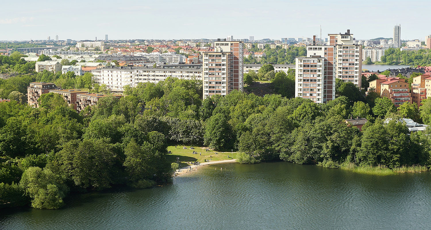En vy över bostadsområde med blandade typer av bostäder, en sjö i förgrunden.